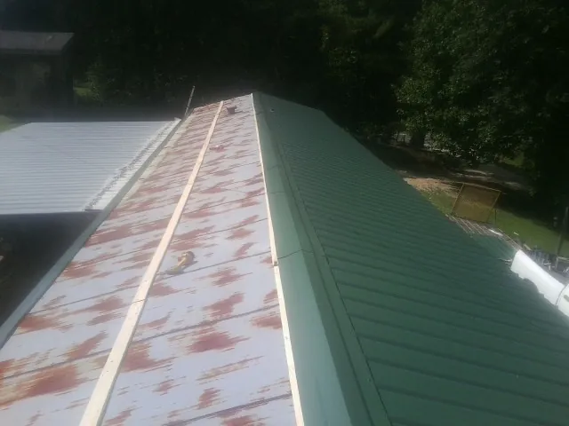 Old rusted panels beside newly installed green metal roofing — Wind Damage Roof Repair by Roofing Brothers in Erwin